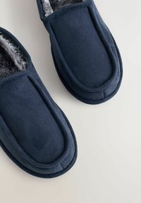 Tumedat sinised sametist sussid pehme halli voodriga, ümarate varvastega ja servadele õmmeldud detailidega. Pehme tekstuur kogu ulatuses.