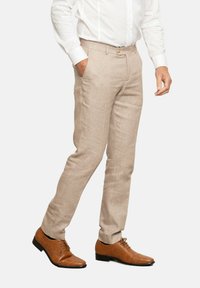 Pantalones de lino color beige claro con un ajuste entallado, que presentan bolsillos laterales y un cierre de botón único. Combinados con zapatos de cuero marrón con cordones.