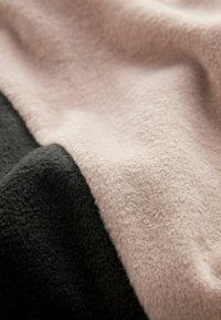 Tejido suave que presenta una sección negra y una sección rosa claro, ambas con una textura peluda y un sutil brillo, mostrando un diseño dividido.