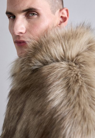Faux fur krave i lyse beige med blød, tæt tekstur. Har et voluminøst, lagdelt design, der hænger omkring halsen.