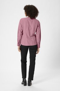 Chemise rose à manches longues avec un col haut, des poignets boutonnés et une coupe décontractée, associée à un pantalon noir et des chaussures à talons bloc.