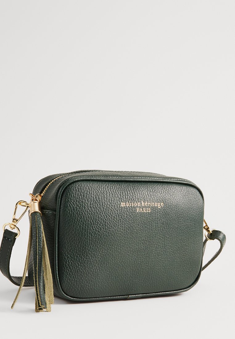 Sac bandoulière en cuir vert avec une surface texturée, quincaillerie dorée et un accent à pompon. Il dispose d'une fermeture éclair et d'une forme rectangulaire.