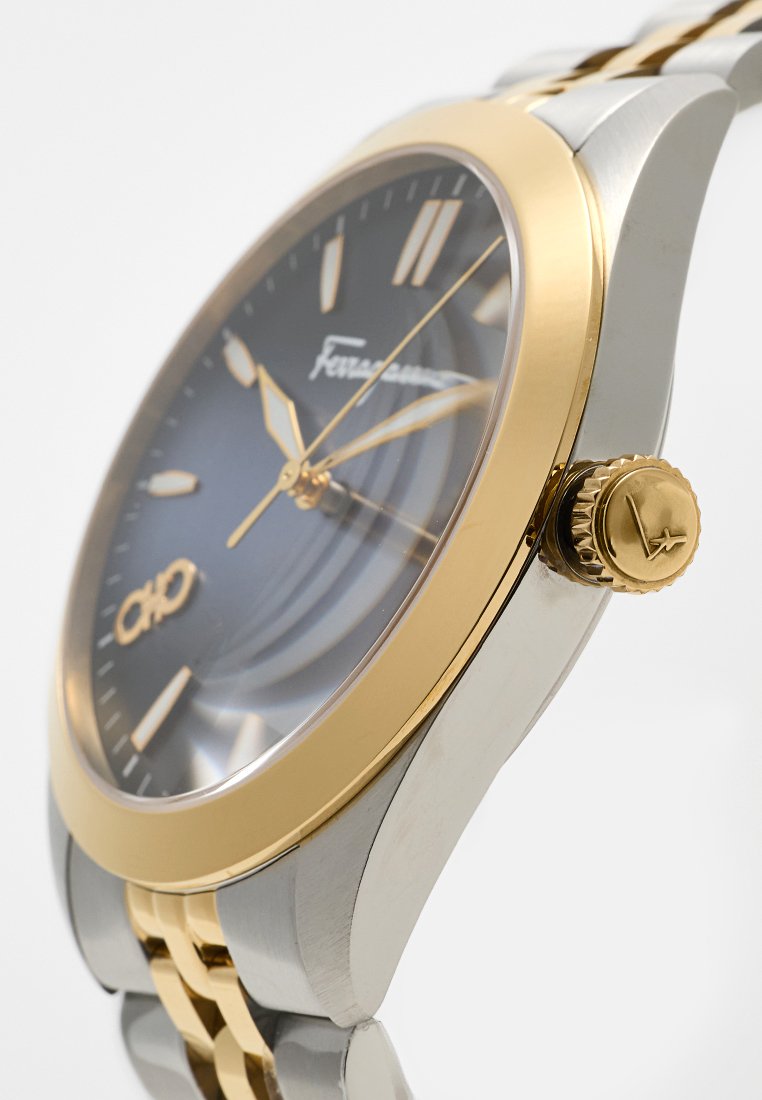 Montre pour hommes avec un cadran gris, des index dorés, un bracelet en acier inoxydable et doré, et une couronne texturée sur le côté.