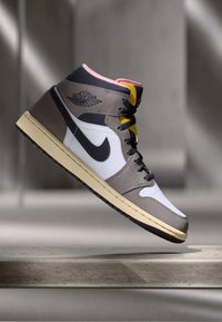 Hohe Nike Air Jordan Sneaker in Weiß, Grau, Schwarz und Pink, die über einer steinernen Oberfläche mit sanfter Hintergrundbeleuchtung schwebt.