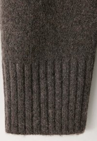 Gros plan sur un poignet de manche en laine tricotée gris foncé avec une texture côtelée sur le bord.