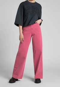 Camiseta de gran tamaño en gris oscuro con el texto "LEE JEANS", combinada con unos pantalones de pierna ancha rosas de alta cintura y zapatos negros de suela gruesa.