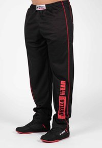 Zwarte sportleggingen met rode accenten, voorzien van een zijlogo-print, een trekkoord in de taille en gemaakt van ademend, textuurmateriaal.