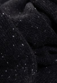Tessuto a maglia nera con un motivo maculato che presenta piccole fibre bianche. La consistenza sembra morbida e leggermente pelosa.