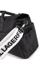 Geantă neagră din nylon cu închidere cu fermoar, având o suprafață texturată. Include o curea detașabilă cu inscripții negre pe fundal alb.