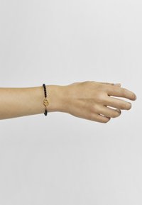 Pulsera de cuentas negras con un broche de acento dorado. Las cuentas son lisas y redondas, creando un contraste texturizado con el brillante hardware dorado.