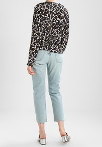 Blusa nera floreale con dettaglio a coulisse, abbinata a jeans azzurri a vita alta e scarpe con tacco alto argentate, mostrata da dietro.
