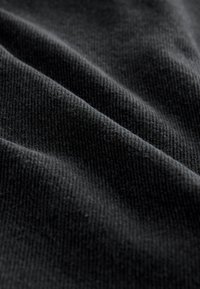 Tessuto nero con superficie morbida e strutturata e motivi a coste visibili, che mostra strati ripiegati e profondità nel colore.