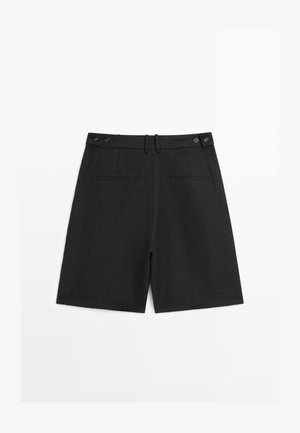 Shorts noirs sur mesure avec ajusteurs latéraux à boutons, passants pour ceinture et deux poches passepoilées à l'arrière, posés à plat sur un fond blanc.