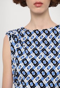 Top fără mâneci multicolor cu un model geometric în albastru, negru și alb, cu o ușoară adunare la cusătura umărului.