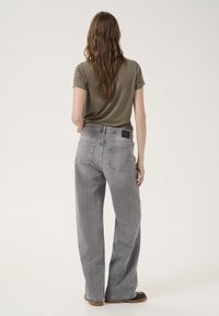 Jeans in denim grigio a gamba larga con una texture sbiadita e cinque tasche. Abbinati a una t-shirt aderente verde oliva e scarpe marroni.