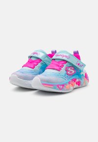 Helle blaue Turnschuhe mit pinken und lila Akzenten, schimmerndem Stoff, Klettverschluss und herzfömigen bunten Sohlen-Details.