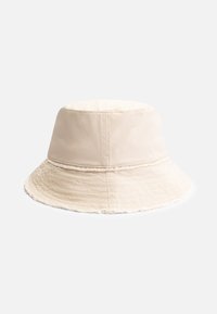 Chapeau seau beige en tissu doux, avec un large bord et des bords effilochés. Présente une texture lisse et légère ainsi qu'un design structuré.