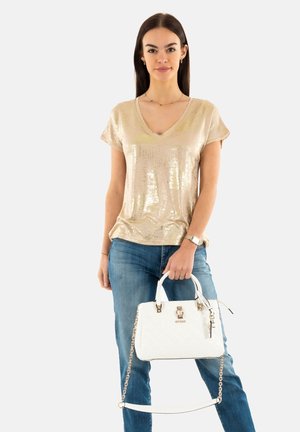Top en sequins dorés avec décolleté en V, jeans bleus et sac à main blanc matelassé avec quincaillerie dorée et bandoulière en chaîne détachable.