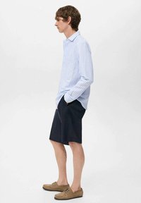 Came shirt a manica lunga a righe blu chiaro e bianche, pantaloni corti blu navy e scarpe color ocra. La camicia presenta un colletto classico e una vestibilità comoda.