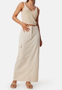 Haut débardeur beige en maille associé à une longue jupe cargo crème avec poches latérales, complété par des sandales légères.