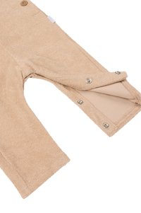 Beżowe ogrodniczki z frotte z zapięciem na napy, teksturowaną powierzchnią i jednym detalem w postaci guzika. Miękki materiał zapewniający komfort i łatwość noszenia.