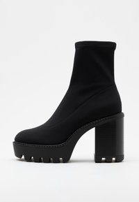 Botas negras hasta el tobillo hechas de un tejido elástico con un diseño de tacón grueso, que presentan una suela texturizada y una silueta sin costuras.