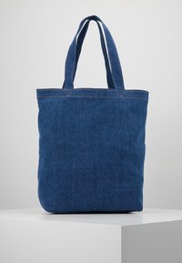 Sac fourre-tout en denim bleu avec deux anses solides, forme rectangulaire et détails de coutures visibles. Design minimaliste, surface épurée.
