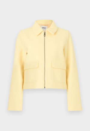 Chaqueta amarilla corta con cremallera frontal, dos bolsillos delanteros y cuello plano. Textura suave y diseño minimalista.