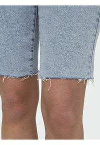 Shorts en denim bleu clair avec un ourlet effiloché, mettant en avant une texture lisse et une coupe ajustée, se terminant au-dessus du genou.