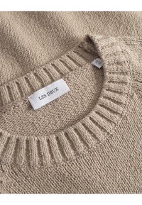 Beige strikkegenser med ribbestrikket rund hals. Merket sier "LES DEUX." Myk tekstur med et grovt strikkemønster.
