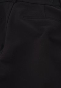 Zwarte broek met een gladde textuur, voorzien van twee achterzakken en een eenvoudige, gestroomlijnde uitstraling. Subtiele stiksels zijn zichtbaar.