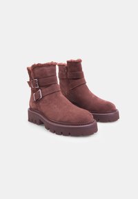 Botas de tobillo de ante marrón con trim de pelo sintético, correas de doble hebilla y una suela de goma rugosa con profundos surcos para mayor tracción.
