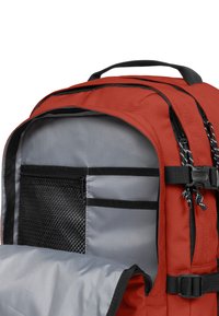 Mochila roja con interior gris, que cuenta con múltiples bolsillos, cremalleras y correas ajustables. Fabricada con un material duradero con un acabado texturizado.