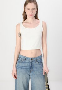 Hvit strikket cropped tank topp med ribbestrikket kant. Kombinert med lyseblå vide jeans. Tilbehør inkluderer en grønn skulderveske.