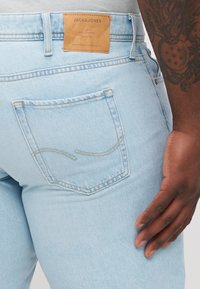 Svijetloplav jeans s tamnom kožnom oznakom na struku. Imaju stražnji džep s zakrivljenom šavom i standardni kroj.