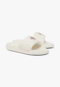White slide sandals made of smooth material, featuring a wide strap and a round logo accent. Black textured sole for grip and comfort.