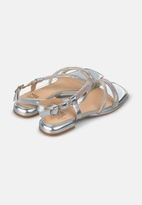 Sandali silver con tacco piatto, caratterizzati da cinturini incrociati decorati con accenti scintillanti e chiusura con fibbia. Finitura metallica liscia.