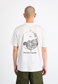 Hvid kortærmet t-shirt med et sort grafisk design på ryggen, der viser et cirkulært mønster og teksten "the new originals."