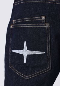 Jeans de mezclilla oscura con un gran diseño de estrella blanca bordada en el bolsillo trasero, acentuados con botones de cobre y costuras doradas.