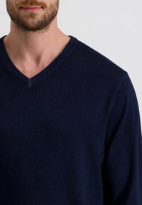 Marineblauwe V-hals trui, gebreide stof, gemiddelde dikte met ribbeltextuur bij de halslijn, nauwsluitend om het bovenlichaam.