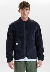 Giacca in pile blu scuro con zip, caratterizzata da una piccola tasca sul petto, texture morbida e vestibilità comoda. Adatta per un abbigliamento informale.
