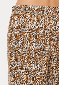 Leopardmönstrad tyg med nyanser av orange, svart och vitt; elastisk midja och slät textur som framhäver intrikata mönsterdetaljer.