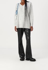 Jasnoszary, oversize sweter z dekoltem w kształcie litery V, z prążkowanymi mankietami, w połączeniu z czarnymi, szerokimi spodniami z faux skóry i czarnymi masywnymi butami.