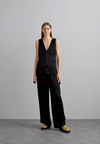 Top nero senza maniche con scollatura a V profonda e tessuto strutturato, abbinato a pantaloni neri larghi e scarpe chunky bicolore in nero e verde.