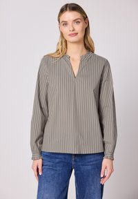Chemise grise à manches longues avec des rayures blanches verticales, un léger col en V et un design de poignets froncés, portée avec un jean bleu.