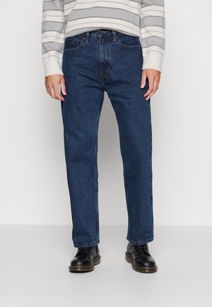 Jeans de mezclilla azul oscuro con corte recto, diseño de cinco bolsillos y detalles de costura sutil, combinados con botas negras de cordones.