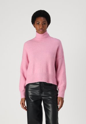 Maglione a collo alto rosa realizzato in morbido tessuto; presenta spalle scese e orlo corto, abbinato a pantaloni in pelle nera eleganti.