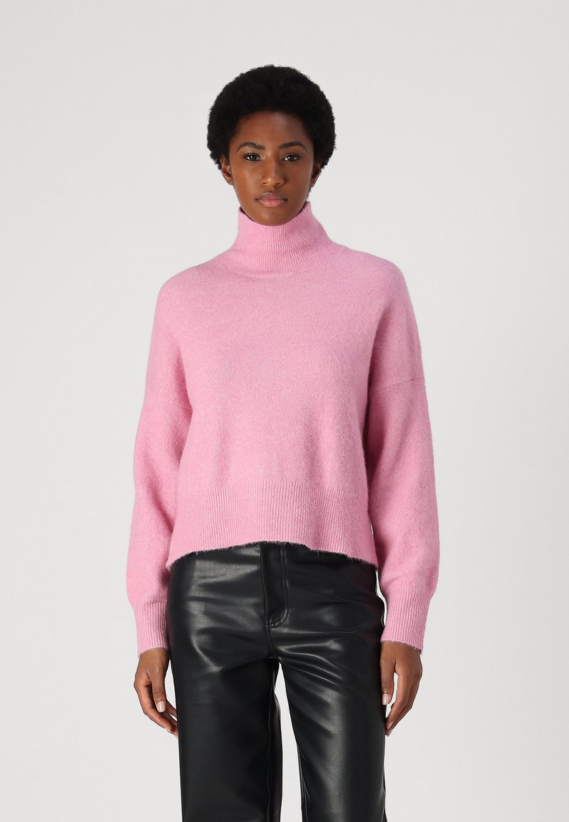 Rosa Rollkragenpullover aus weichem Stoff; mit fallenden Schultern und einem verkürzten Saum, kombiniert mit eleganten schwarzen Lederhosen.