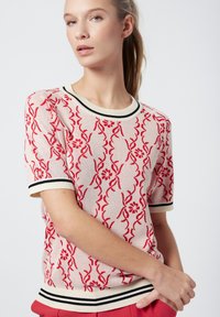 Suéter de punto en crema con patrón floral rojo, cuello y puños de rayas en negro y crema. Mangas cortas, corte relajado.