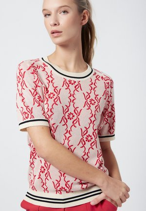 Maglione lavorato a maglia in crema con motivo floreale rosso, colletto e polsini a righe nere e crema. Maniche corte, vestibilità comoda.